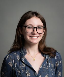 headshot of a women with brown hair and glasses in front of a grey background